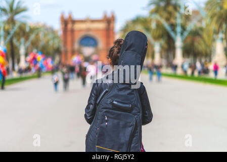 Vista posteriore di una giovane ragazza hippster donna che cammina in un parco nella giornata di sole mentre porta una chitarra sul retro Foto Stock