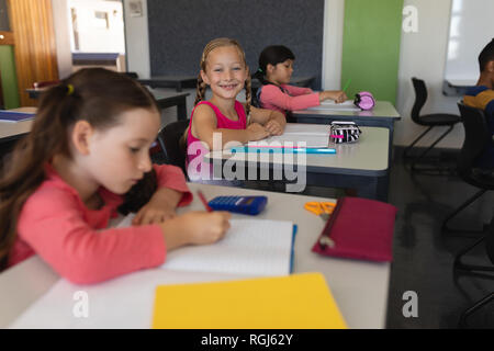 Schoolgirl guardando la fotocamera mentre studiano in aula Foto Stock