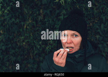 Donna applicando balsamo per labbra in fuori strada in una fredda giornata invernale contro la comune parete di edera Foto Stock