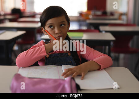 Riflessivo schoolgirl studiare in aula seduto alla scrivania nella scuola Foto Stock