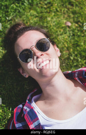 Vista dall'alto di un giovane hipster sorridente Donna sdraiata sull'erba in una giornata di sole in un parco mentre si prende un selfie con un telefono cellulare Foto Stock