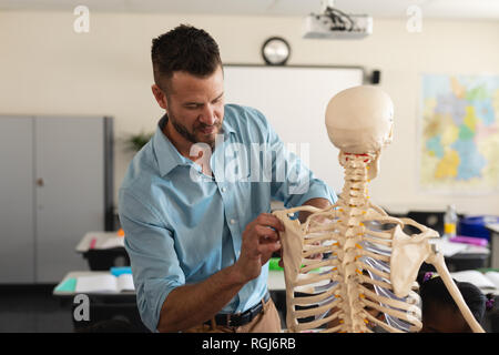 Insegnante di sesso maschile che fissa il modello dello scheletro in aula Foto Stock