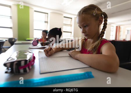 Vista laterale di schoolgirl studiando al banco in aula Foto Stock