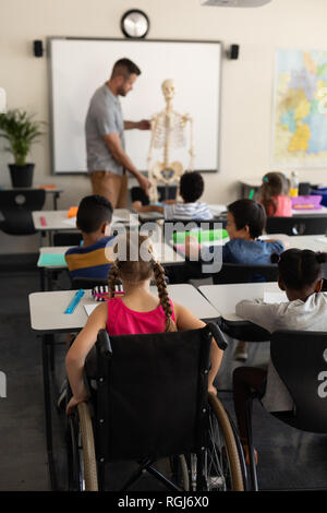 Vista posteriore di disabilitare schoolgirl con un compagno di classe a studiare in aula seduto al banco di scuola elementare Foto Stock