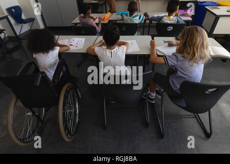 Angolo di alta vista di disabilitare schoolgirl con i compagni di classe di studiare e seduti alla scrivania in aula Foto Stock