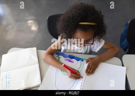 Angolo di alta vista schoolgirl disegno nel libro in aula Foto Stock