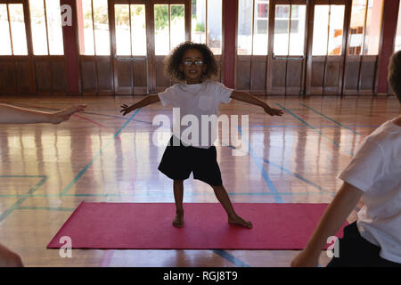 Schoolgirl fare yoga su un materassino yoga nella scuola Foto Stock