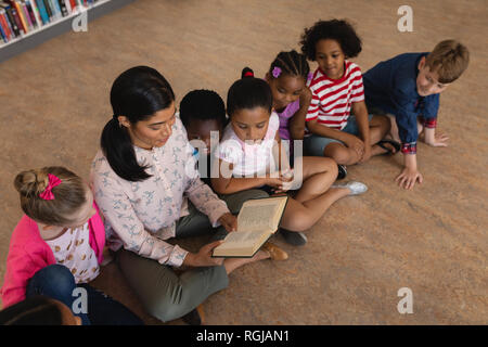 Angolo di alta vista di insegnante femmina schoolkids insegnamento e seduto sul pavimento della biblioteca della scuola Foto Stock