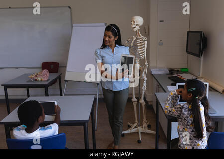 Vista frontale femmina insegnamento insegnante scolaro sulla tavoletta digitale a tavola in aula della scuola elementare Foto Stock