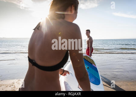 Francia, Bretagna, coppia giovane che trasporta un SUP PENSIONE al mare insieme Foto Stock