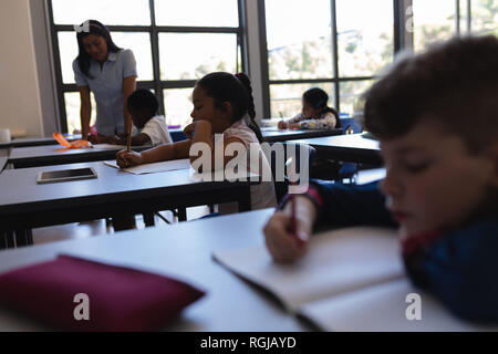 Giovani femmine insegnante insegnamento schoolkid al banco in aula della scuola elementare Foto Stock