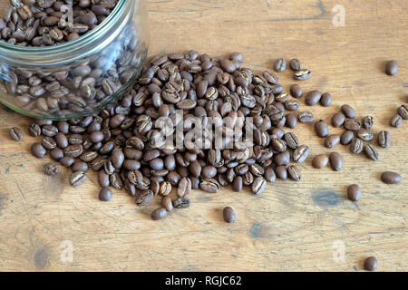 Partita di caffè torrefatto in grani sparsi nei pressi di rotondo in vetro trasparente vaso su un vecchio tavolo di legno vista da vicino Foto Stock