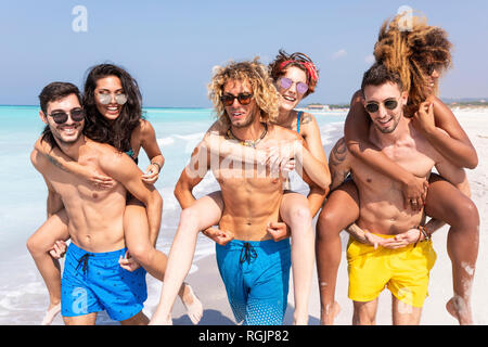 Gli amici di camminare sulla spiaggia, portando fidanzate piggyback Foto Stock