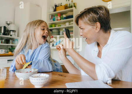 Felice madre e figlia divertirsi a tavola a casa prendendo immagini dello smartphone Foto Stock