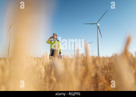 Ingegnere in piedi in un campo di una fattoria eolica parlando al cellulare