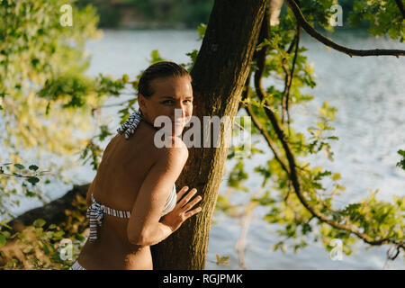 Ritratto di donna sorridente indossando un bikini a tronco di albero in un lago Foto Stock