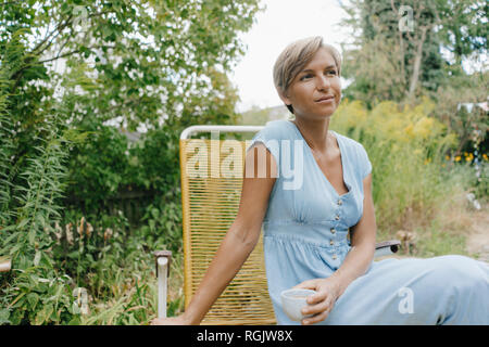 Donna seduta in giardino con tazza di caffè Foto Stock