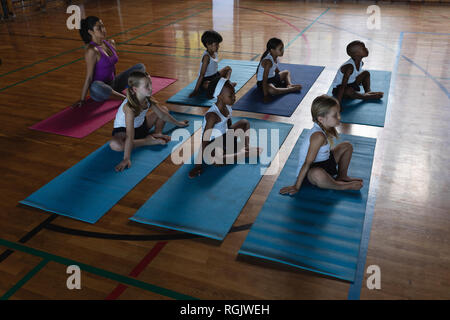 Elevato angolo di visione femminile di insegnante di yoga e schoolkids praticare lo yoga e la meditazione un materassino yoga nella scuola Foto Stock