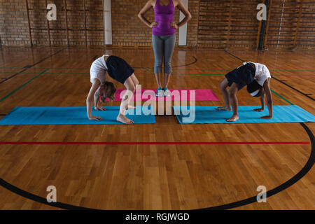 Femmina insegnante di yoga e schoolkids fare yoga su un materassino yoga nella scuola Foto Stock