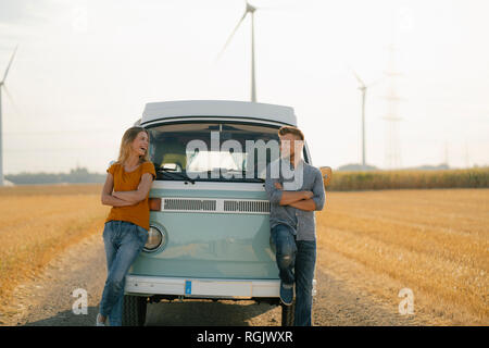 Coppia felice a camper van nel paesaggio rurale con le turbine eoliche in background Foto Stock