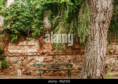 Il vecchio grunge rotto in legno panca su cariati Mattoni abbandonati parete rurale sfondo nel piccolo paese trascurato village Foto Stock