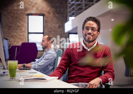Giovane uomo seduto alla scrivania in ufficio, sorridente Foto Stock