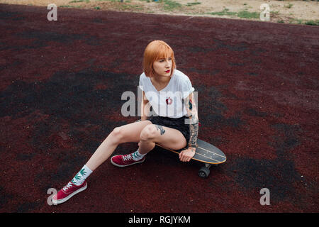 Giovane donna seduta su carver skateboard all'aperto Foto Stock