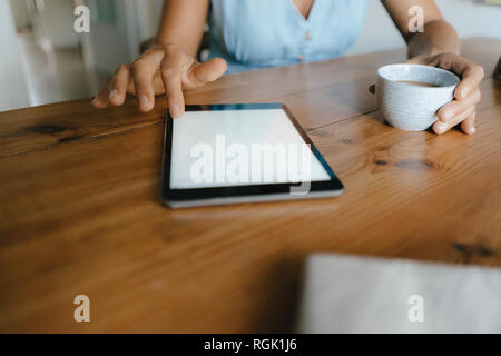 Close-up di donna seduta a tavola a casa con la tazza di caffè e tablet Foto Stock