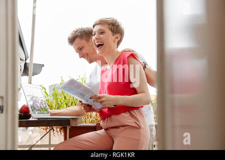 Coppia felice sul balcone a casa con il computer portatile e la mappa Foto Stock