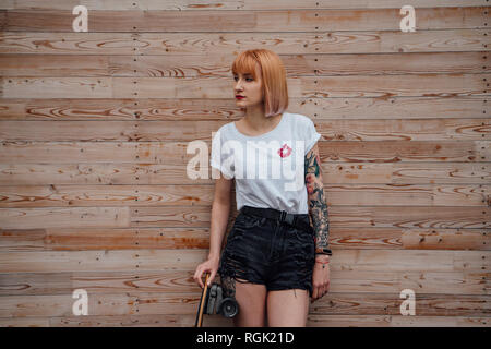 Giovane donna in piedi alla parete in legno con lo skateboard Foto Stock