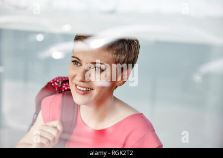 Ritratto di donna sorridente con zaino dietro il vetro di finestra Foto Stock