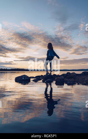 Giovane donna in piedi al lago Inari, con le braccia aperte, Finlandia Foto Stock