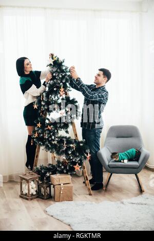Giovani carino coppia decorare un albero di Natale alla vigilia di Natale. Foto Stock