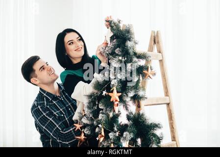 Giovani carino coppia decorare un albero di Natale alla vigilia di Natale. Foto Stock