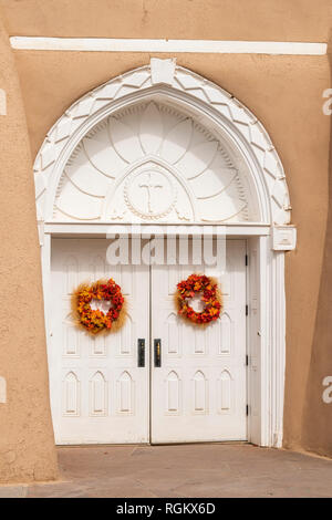 Ghirlande colorate sulle bianche scolpite le porte di ingresso a San Francisco de Asis chiesa in Ranchos de Taos, Nuovo Messico, STATI UNITI D'AMERICA Foto Stock