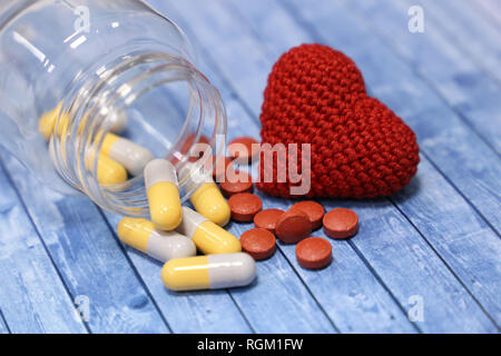 Pillole, capsule, rosso cuore di maglia e la bottiglia di plastica blu sul tavolo di legno. Concetto di malattia cardiaca, polypharmacy, pressione sanguigna, Polypharmac Foto Stock