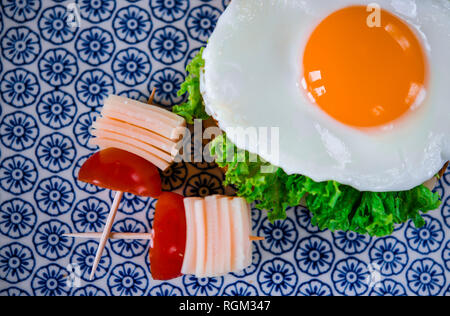 Buona mattina. La deliziosa prima colazione con panino con uova, prosciutto, formaggio, toast e foglie di insalata si trova su una piastra con pomodoro e aneto Foto Stock