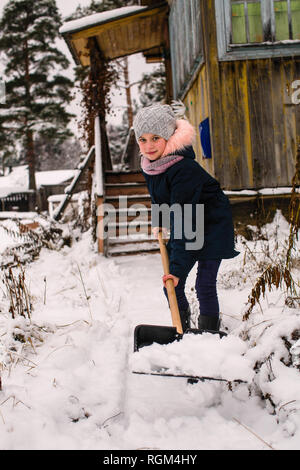 Ragazza carina pulisce la neve a pala vicino alla casa di campagna. Foto Stock