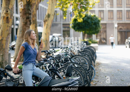 Paesi Bassi, Maastricht, sorridente ragazza bionda tenendo cono gelato in città al rack per bicicletta Foto Stock