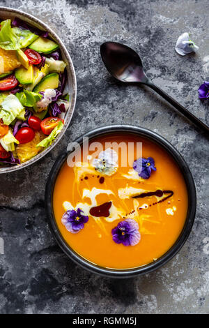 Ciotola di insalata mista con fiori commestibili e una ciotola di crema di zuppa di zucca guarnito con fiori commestibili Foto Stock