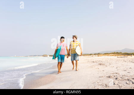 Gli amici di camminare sulla spiaggia, portando le tavole da surf Foto Stock
