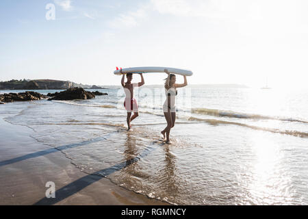 Francia, Bretagna, coppia giovane che trasporta un SUP PENSIONE al mare insieme Foto Stock