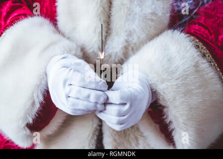 Le mani di Babbo Natale azienda burning sparkler, close-up Foto Stock