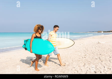 Paio di camminare sulla spiaggia, portando le tavole da surf Foto Stock