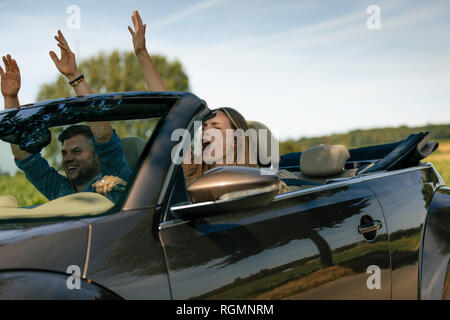 Coppia felice guida con sollevamento darms convertibile in auto sulla strada di un paese Foto Stock