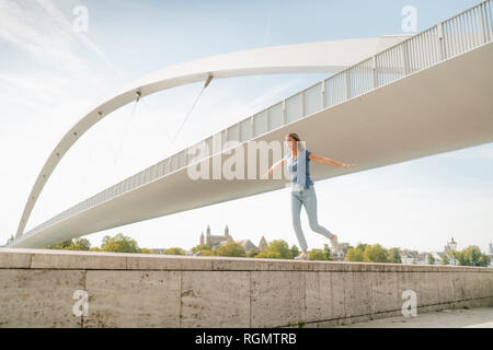 Paesi Bassi, Maastricht, giovane donna in equilibrio su una parete in corrispondenza di un ponte Foto Stock