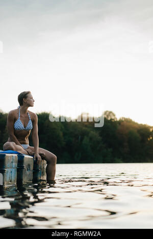 Donna che indossa un bikini seduta su un galleggiante in un lago Foto Stock