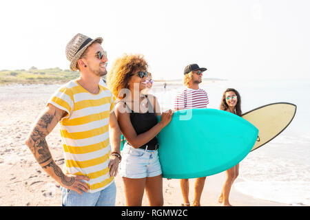 Gruppo di amici di camminare sulla spiaggia, portando le tavole da surf Foto Stock