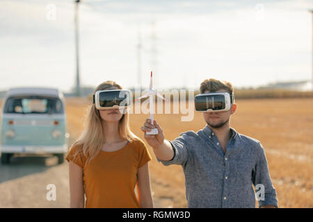 Coppia giovane con occhiali VR a camper van nel paesaggio rurale azienda vento modello di turbina Foto Stock