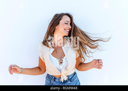 Felice giovane donna scuotendo i suoi capelli nella parte anteriore del muro bianco Foto Stock